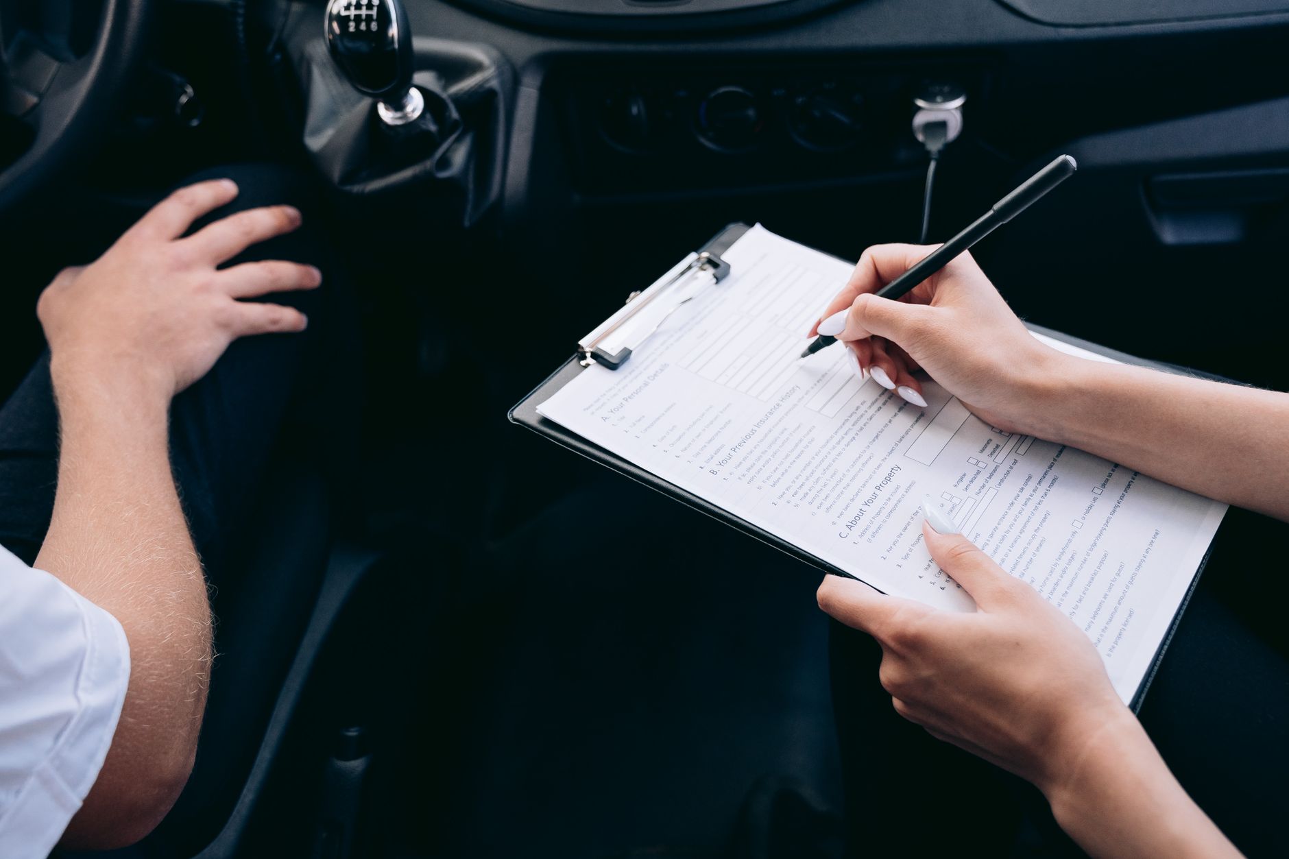 mains remplissant un formulaire posé sur un porte-bloc, à l'intérieur d'une voiture