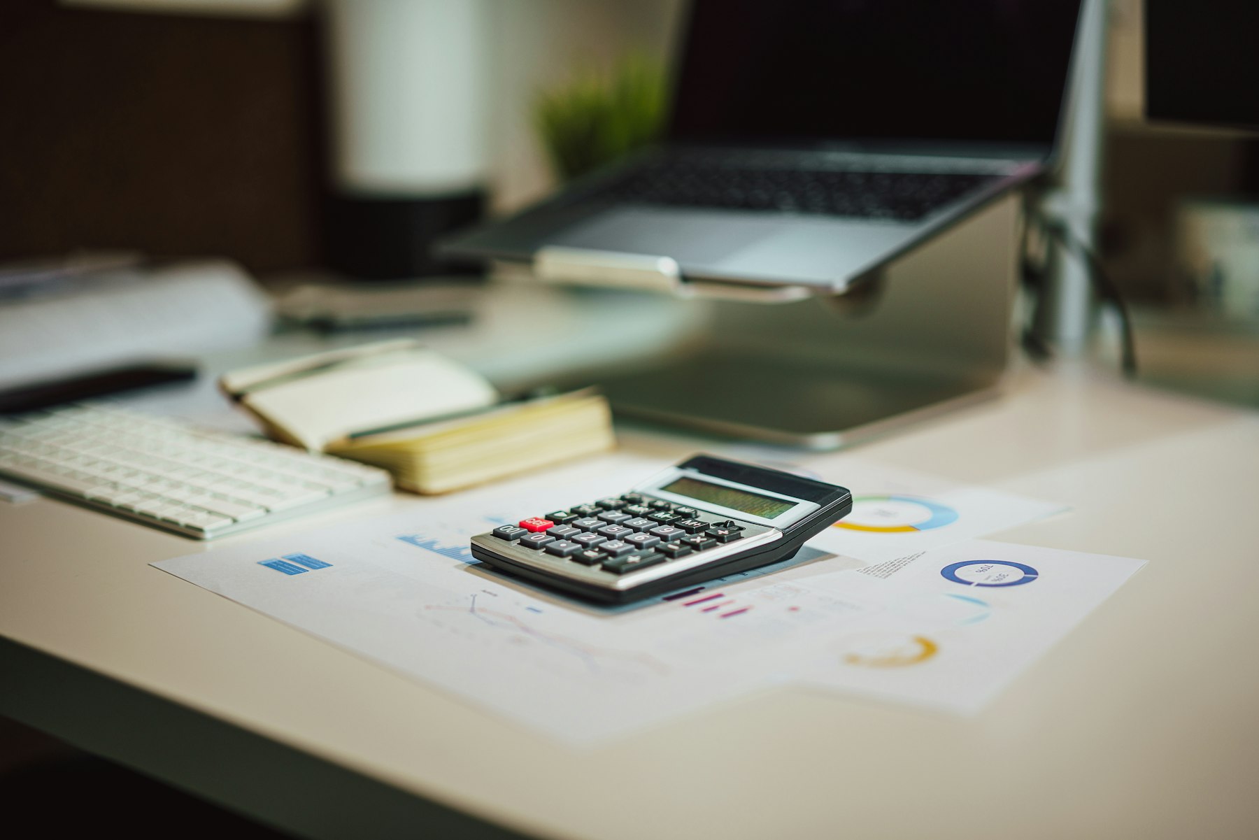 calculatrice, graphiques financiers et ordinateur portable posés sur un bureau, pour estimer un montant de versement PER