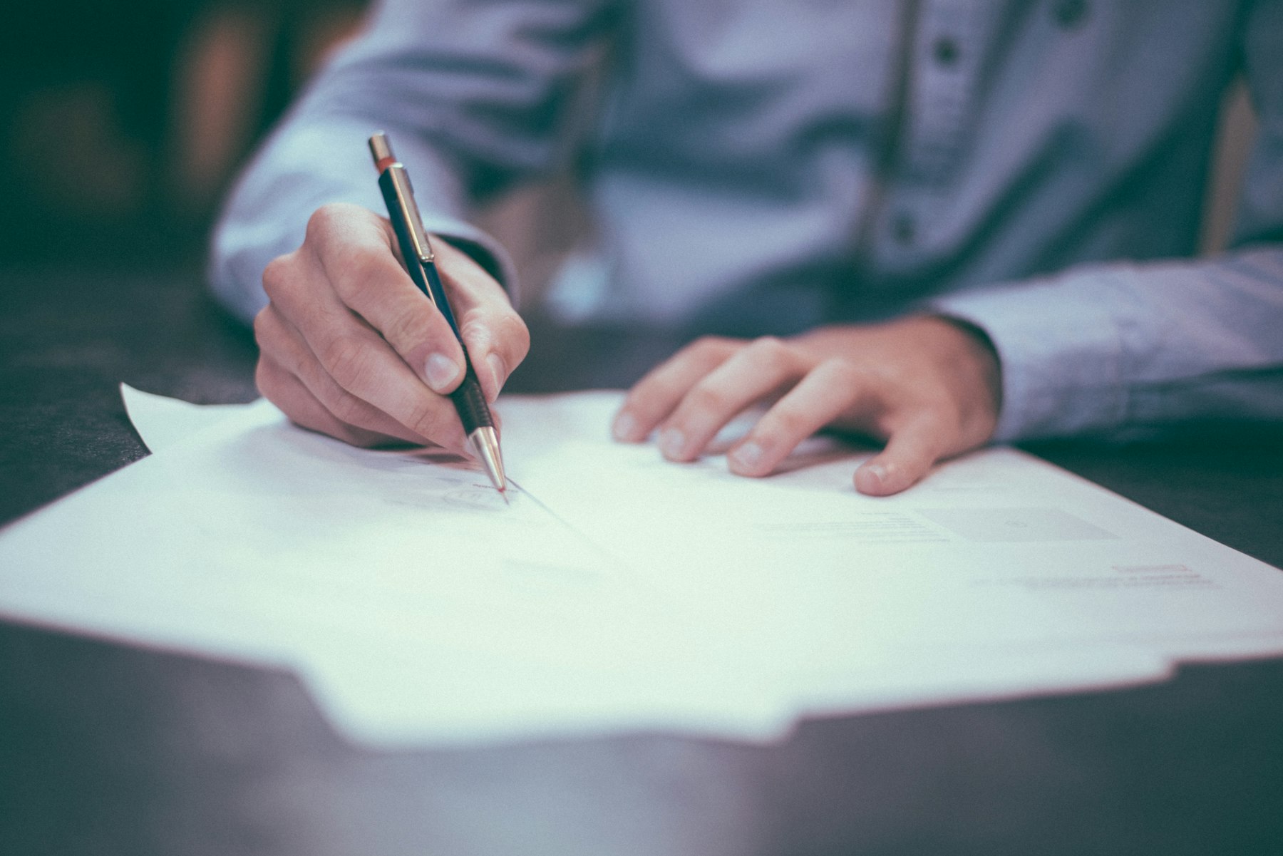 gros plan sur une main qui signe un document papier avec un stylo, pour une déclaration de versements PER