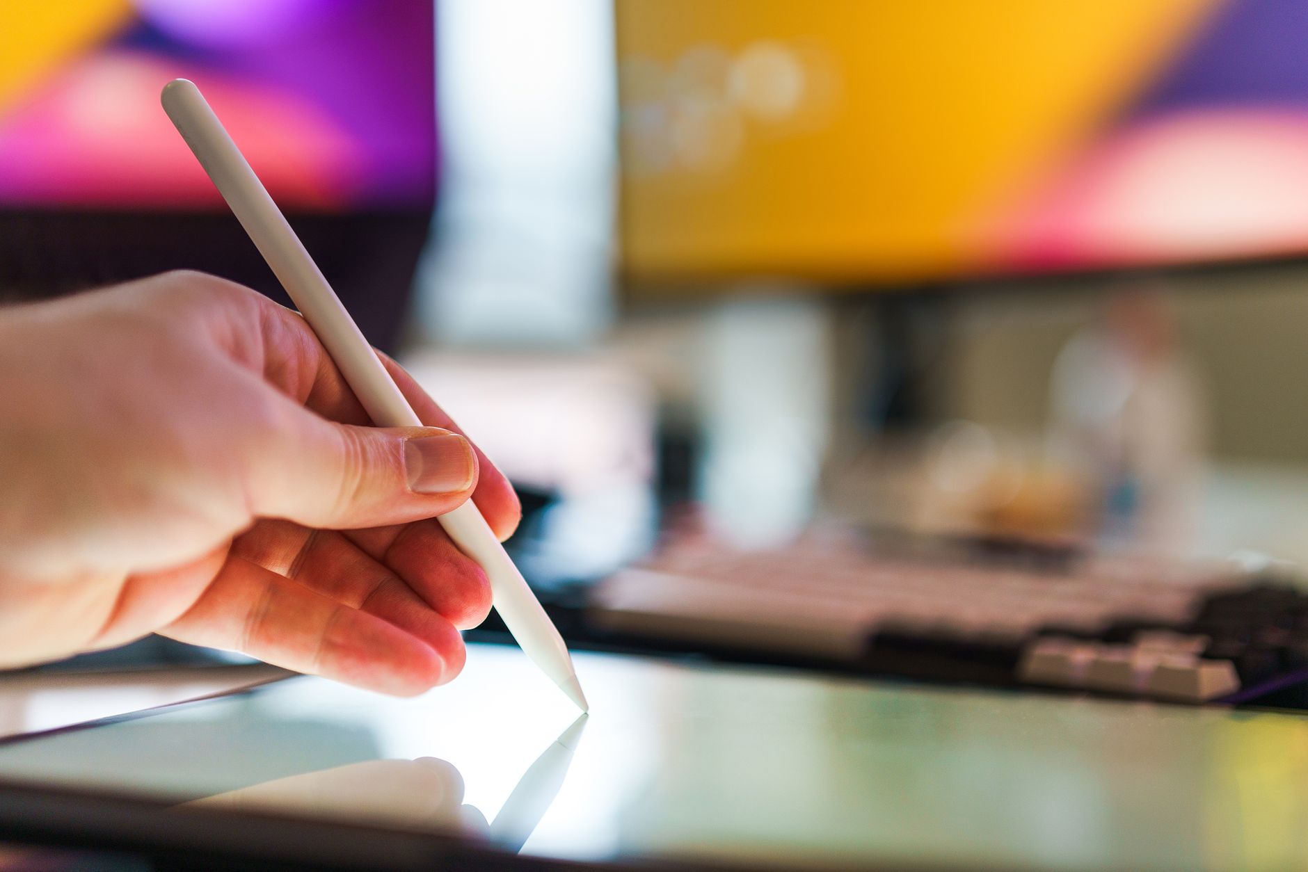 main tenant un stylet au-dessus de l'écran d'une tablette posée sur un bureau