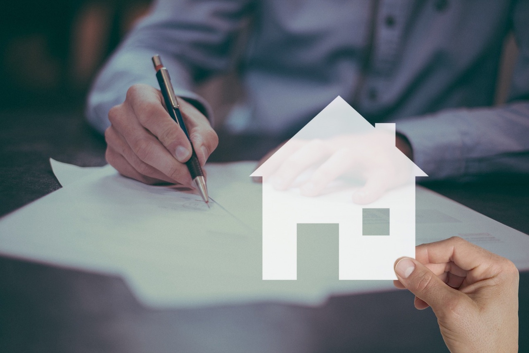 signature d'un document avec une silhouette de maison en papier tenue par une autre main, symbole du compromis de vente