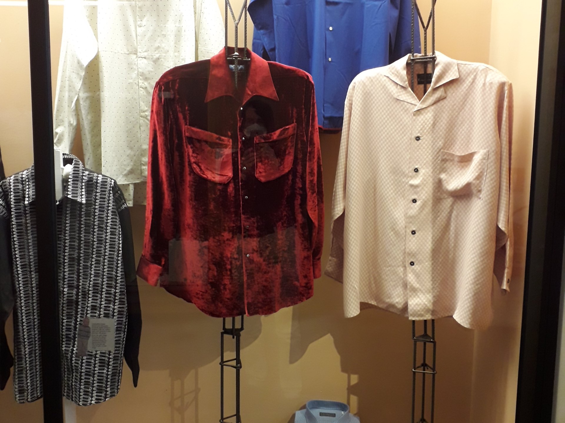 chemises homme exposées sur des bustes en vitrine, une en velours rouge, une en soie claire, une rayée noir et blanc